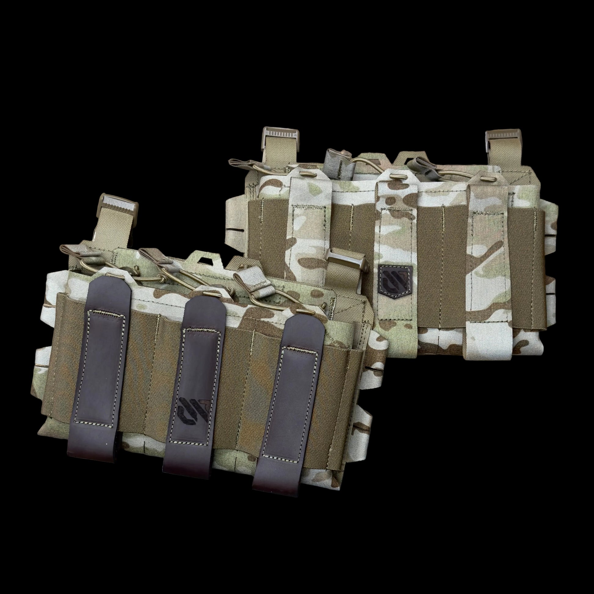 Two tactical utility pouches in camouflage fabric with brown leather loops, laid flat on a worn metal surface.